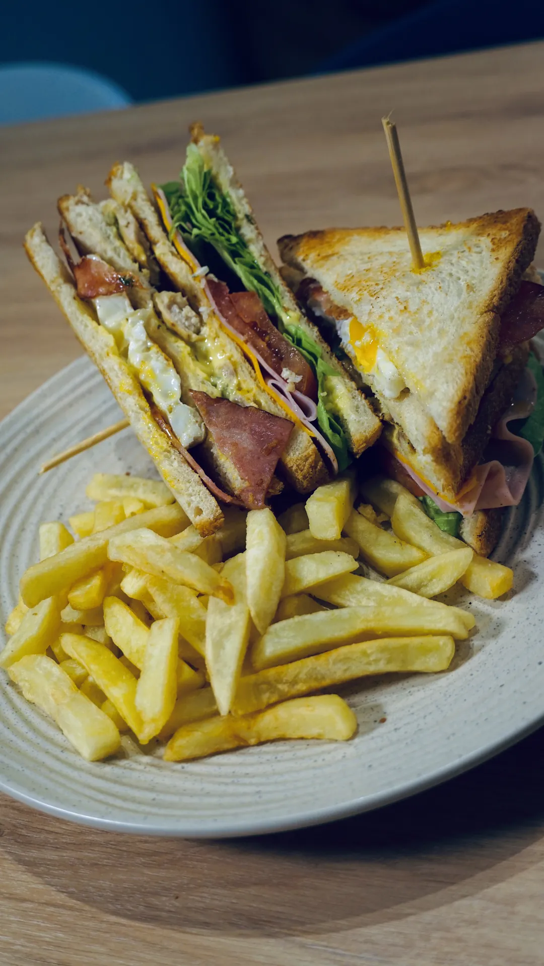 Club sándwich con papas fritas en la barra de un bar, con luces cálidas al fondo