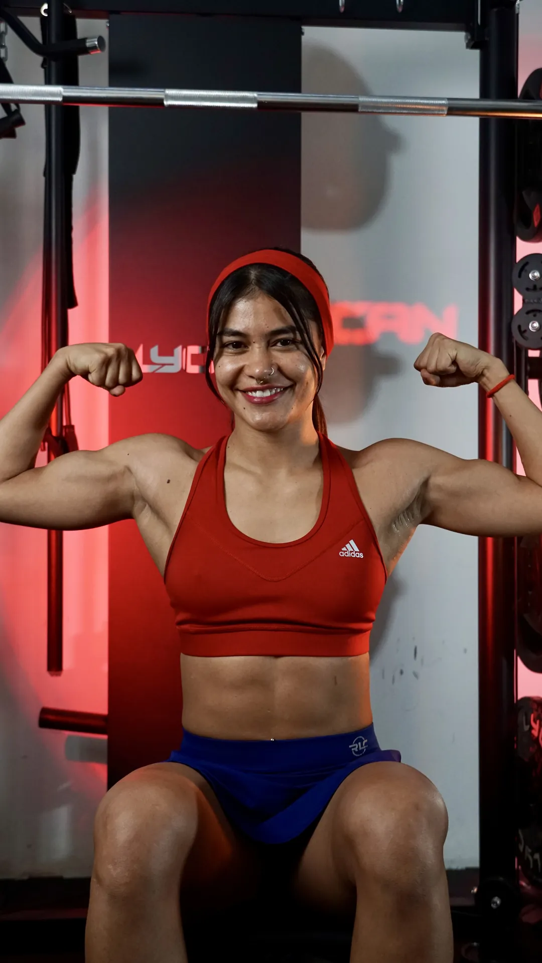 Atleta mostrando los bíceps frente al rack del gimnasio, con luz roja