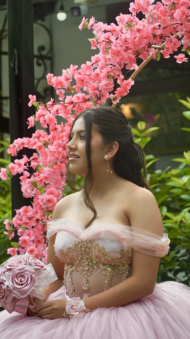 Quinceañera sonriendo entre ramas de flores rosadas