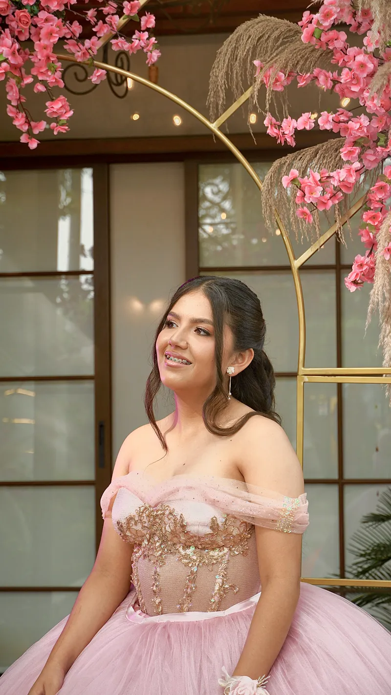 Quinceañera con vestido rosa frente a un arco de flores