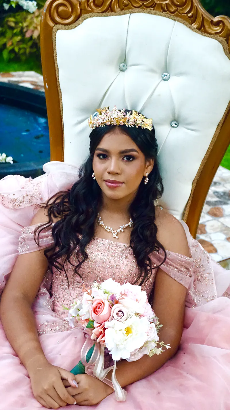 Quinceañera con corona sentada en un sillón blanco y dorado