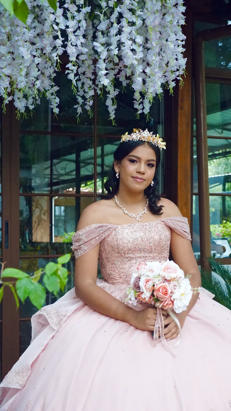 Quinceañera con ramo de flores bajo una cortina de flores blancas